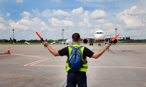 The traffic controller at the airport shows the semaphore with sticks to the pilot of the plane where to park. Arrival of the plane on the runway. Handling service