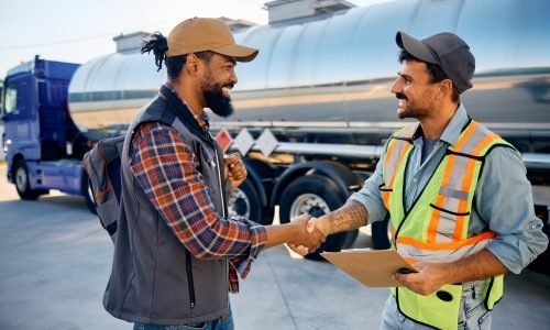 Happy African American truck driver greeting freight transportation manager on a parking lot.